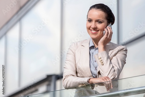 Happy young businesswoman using cell phone at office railing