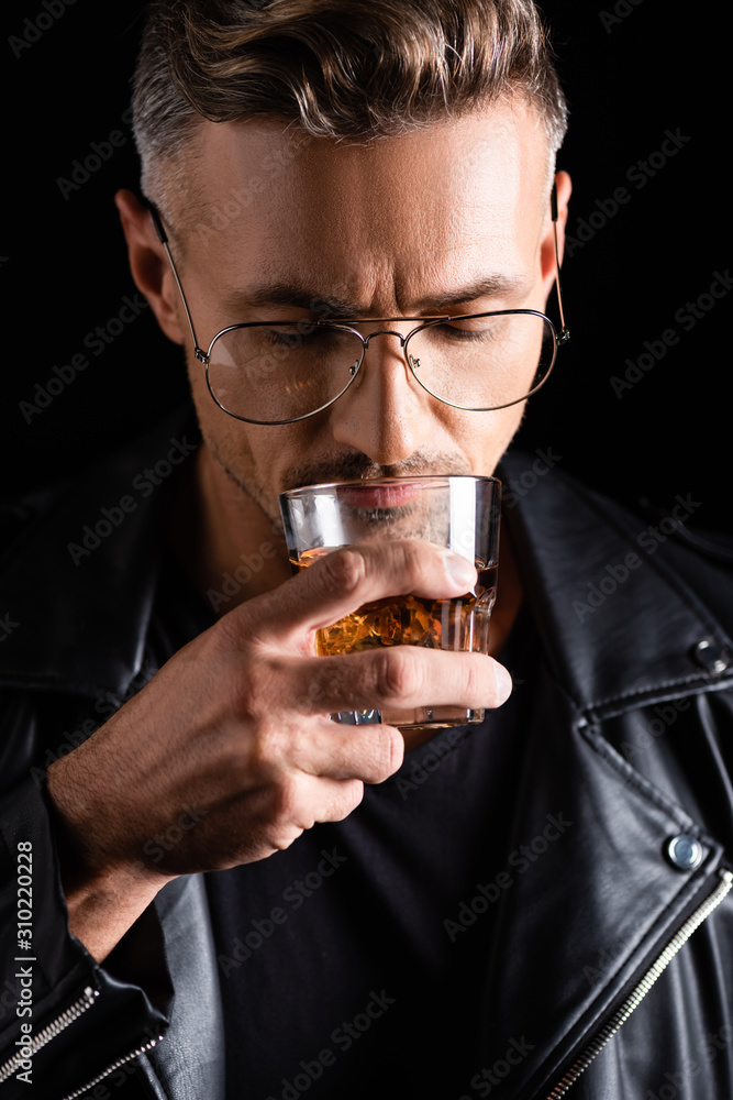Handsome man in sunglasses drinking whiskey isolated on black