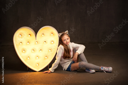 young beautiful blonde in a white sweater with long hair and clean skin and jeans in leggings sits on the floor and smiles