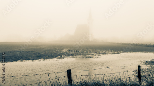Autumn foggy morning, church of Den Hoorn behind the barbed wire. Texel island in the Netherlands, tinted photo