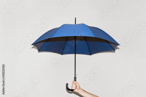 A man holds a blue umbrella in his hand against a gray wall. Concept autumn, color of the year 2020, business, protection