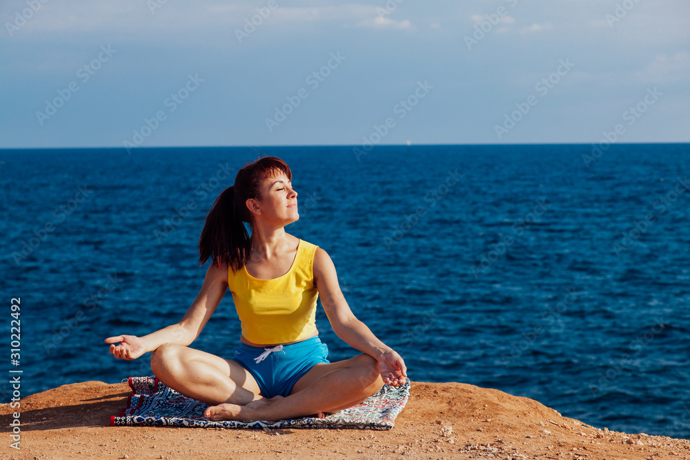 Fototapeta premium the girl is engaged in yoga sits on the cliff by the sea