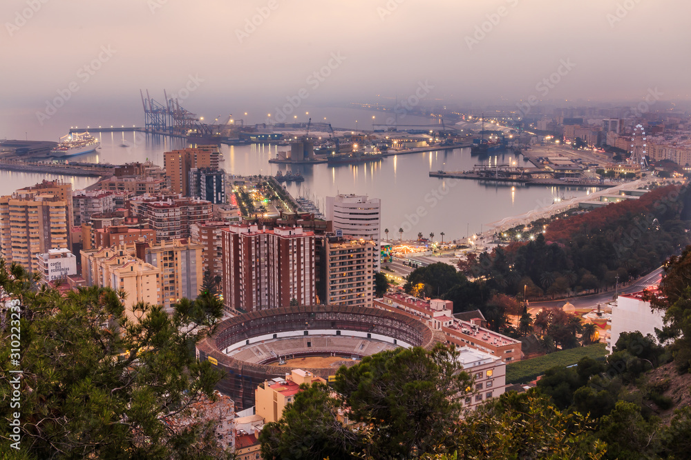 View of the center of the Spanish city of Malaga on the Mediterranean coast. View of the city on the Costa del Sol in the evening with illuminated harbor, residential buildings, trees, street lamps