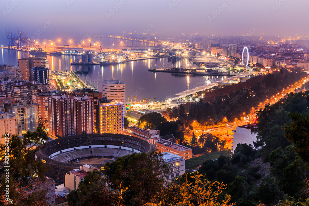Panoramic view at night from Malaga on the Spanish Mediterranean coast. City view on the Costa del Sol with illuminated harbor, residential buildings, trees, street lamps, ferris wheel, ships
