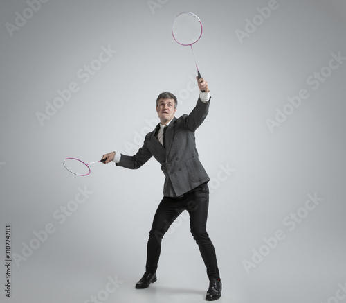 Time for emotions. Man in office clothes plays badminton with two racket on grey background. Businessman training in motion, action. Unusual look for sportsman, activity. Sport, healthy lifestyle. © master1305
