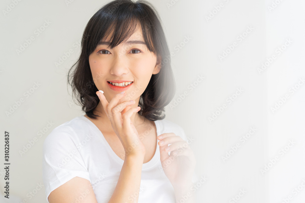 close up young beautiful japanese teenager girl smile with wellness and using moisturizer or UV protection cream on finger to apply on face at inside bedroom in the morning for daily lifestyle concept close up young beautiful japanese teenager girl smile with wellness and using moisturizer or UV protection cream on finger to apply on face at inside bedroom in the morning for daily lifestyle concept