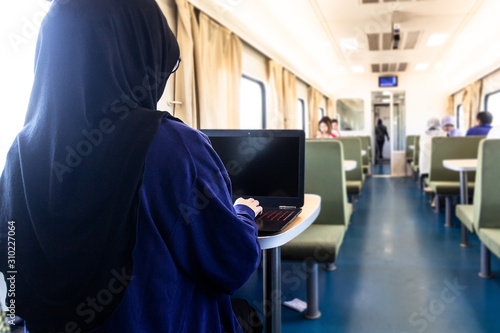 Thai young muslim female freelancer wearing hijab working with laptop on a train or railway during trevelling time. photo