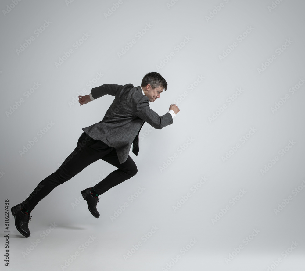 Hurry up, you're wild and young. Caucasian man in office clothes running like a professional sportsman on grey background. Businessman training in motion, action. Sport, healthy lifestyle concept.