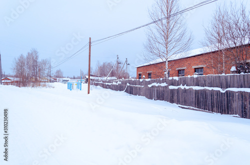 winter village in the snow on a sunny day. street of wooden houses road at houses near the forest, no people. Siberian.