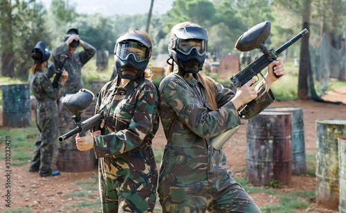 Portrait of confident female paintball players with marker guns outdoors