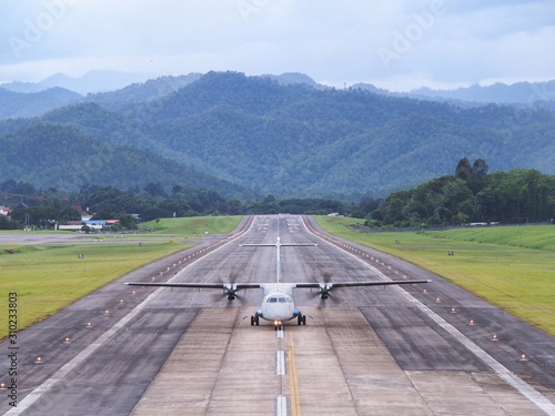 An Airplane / Aeroplane Was Taxiing, Landing, or Taking off on Runway in The Airport Surrounded by Mountains or Hills.