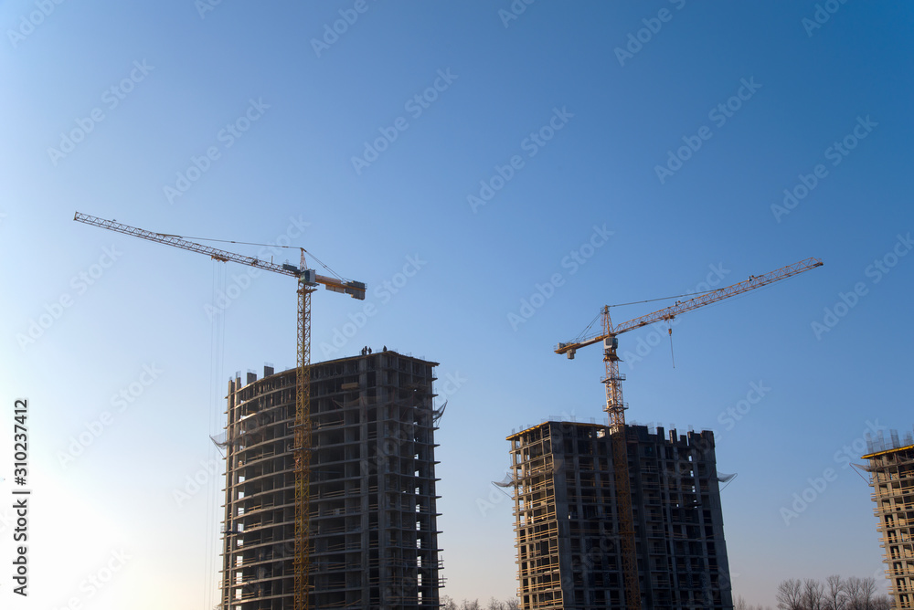 Tower cranes constructing a new residential building at a construction site against blue sky. Renovation program, development, concept of the buildings industry. Tower cranes constructing a new residential building at a construction site against blue sky. Renovation program, development, concept of the buildings industry.