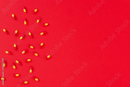 Red-orange pills in capsule on red background, flat lay, top view, copy space