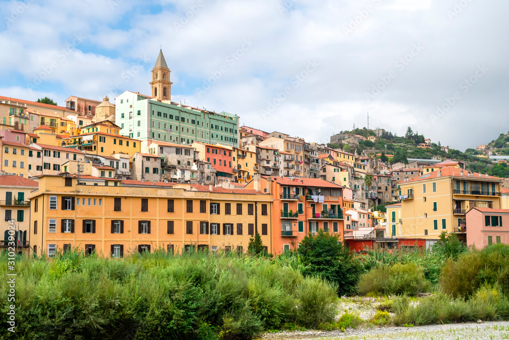 Colorful residential buildings are stacked on a hillside underneath the Ventimiglia Cathedral in the seaside town of Ventimiglia, Italy.