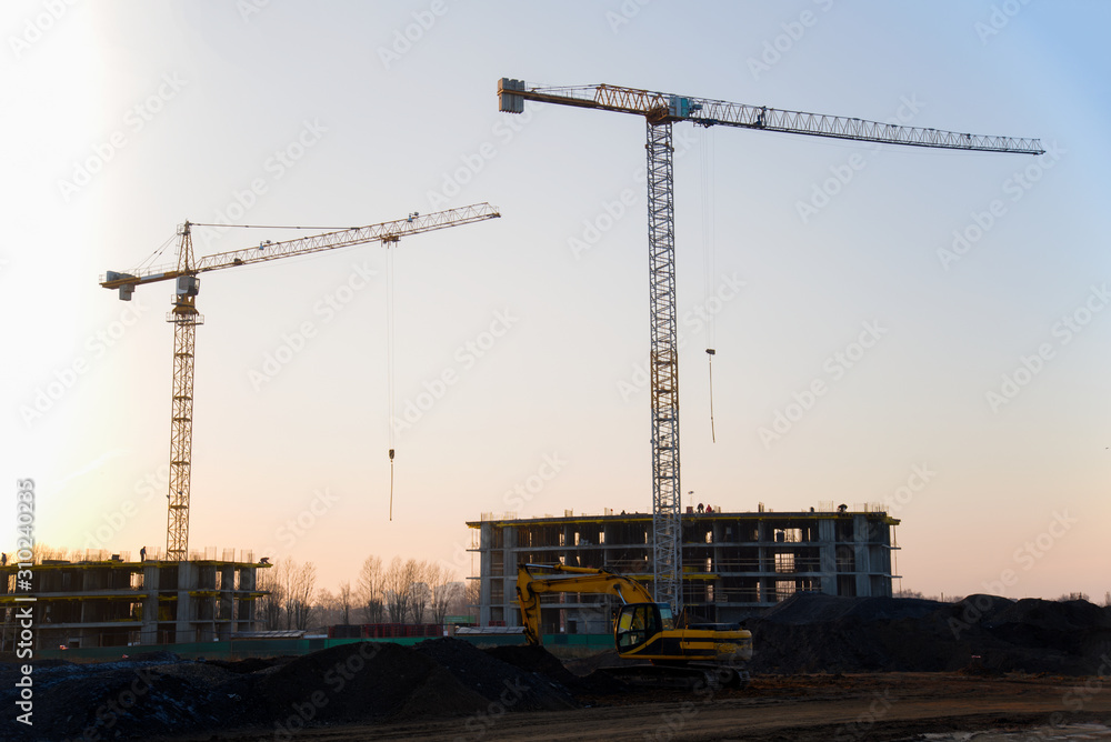 Tower cranes constructing a new residential building at a construction site against blue sky. Renovation program, development, concept of the buildings industry. Tower cranes constructing a new residential building at a construction site against blue sky. Renovation program, development, concept of the buildings industry.