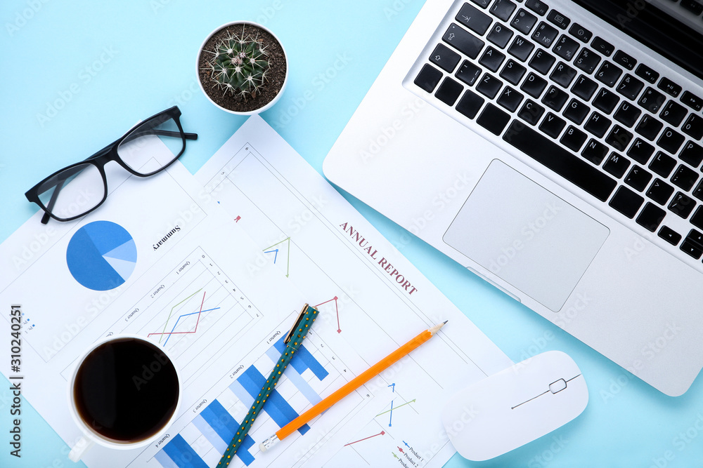 Laptop computer with paper charts and cup of coffee on blue background Laptop computer with paper charts and cup of coffee on blue background