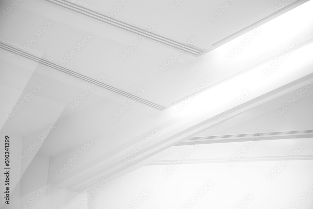 Ceiling and glowing girders with lamps. Abstract architecture fragment. Modern office building interior with triangular white concrete elements. Diagonal geometric composition in light gray halftones. Ceiling and glowing girders with lamps. Abstract architecture fragment. Modern office building interior with triangular white concrete elements. Diagonal geometric composition in light gray halftones.