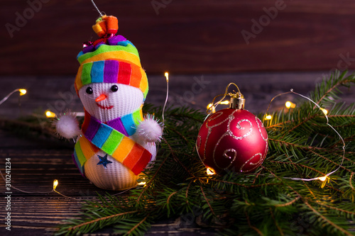 Snowman is not big, on a wooden background. he is wearing a scarf and hat. Christmas tree decoration at the bottom of the spruce photo