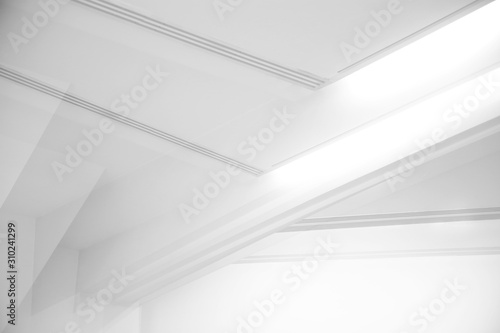 Ceiling and glowing girders with lamps. Abstract architecture fragment. Modern office building interior with triangular white concrete elements. Diagonal geometric composition in light gray halftones.