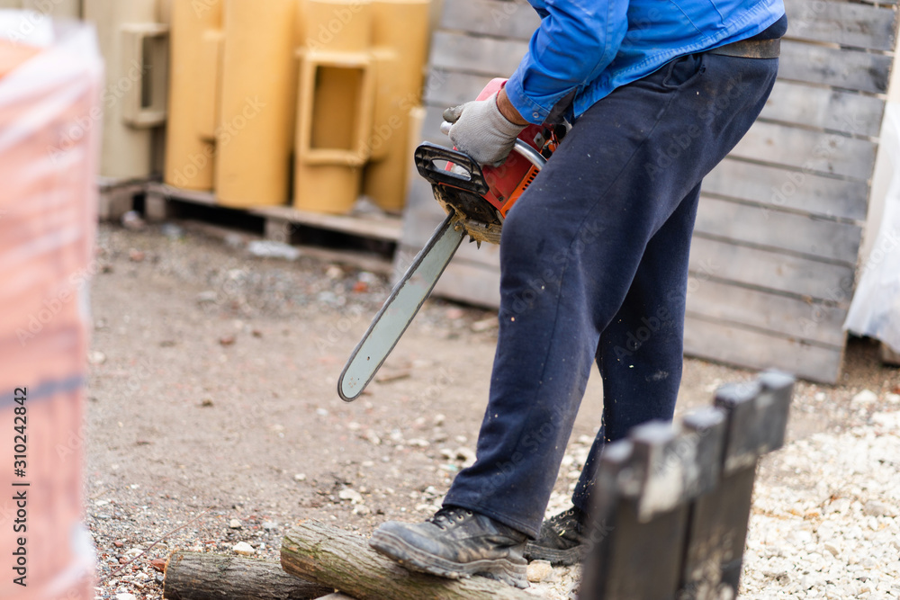 Midsection of man holding the chainsaw cutting wood timber trunk in autumn or winter day in the yard outdoor Midsection of man holding the chainsaw cutting wood timber trunk in autumn or winter day in the yard outdoor