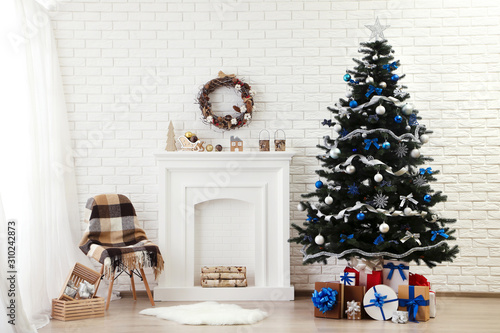 Christmas fir tree with ornaments and gift boxes near decorated fireplace at home