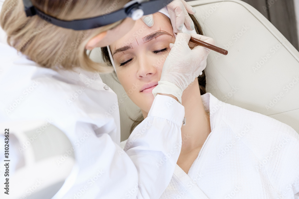Microblading in beauty salon. Hands of an unidentified master make a preliminary drawing with a pencil for a young girl client Microblading in beauty salon. Hands of an unidentified master make a preliminary drawing with a pencil for a young girl client