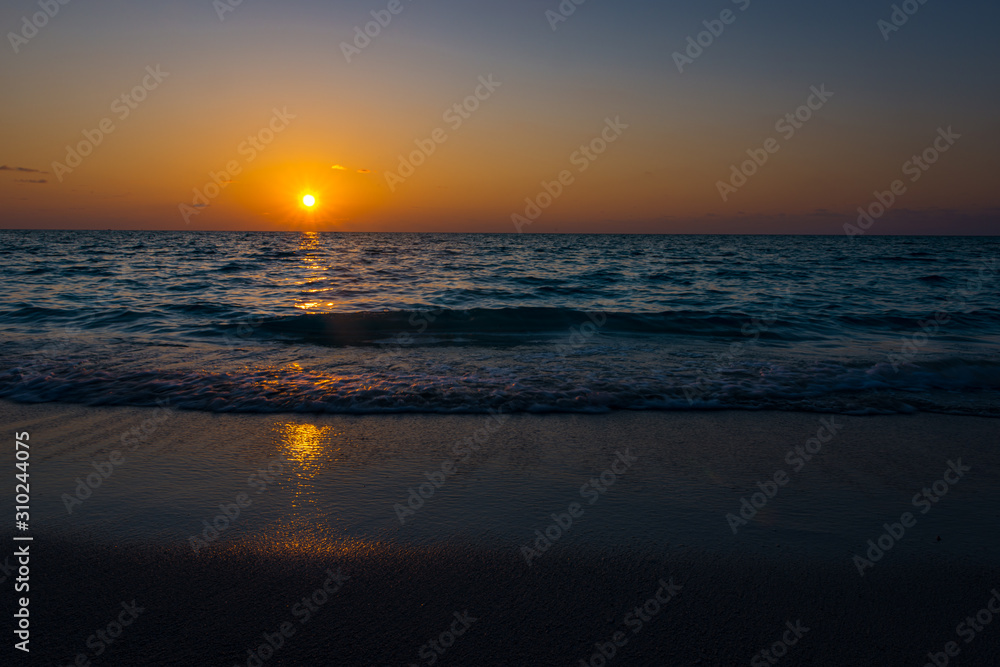 Obraz premium susnet over the ocean, the light is reflecting in the sea while the sun sets farway on the horizon 