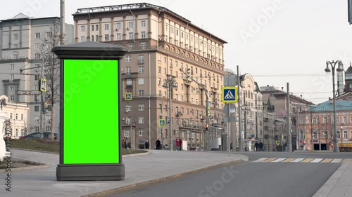 Winter day. City street. A showcase with a green screen stands against the backdrop of large beautiful buildings. Riding cars. Passers-by are coming.
