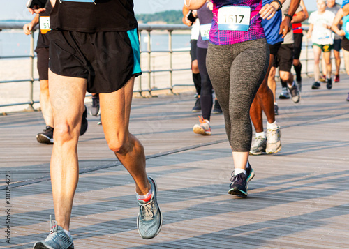 Fototapeta Naklejka Na Ścianę i Meble -  Legs of runners running a race on a boardwalk on a beach