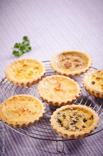 Six different and saborous quiches, on top of a grill grid in a purple tablecloth