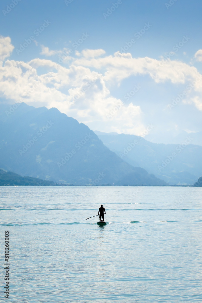 Silhouette of a man standing on a paddleboard on Lake Brienz in Switzerland. Mountains in the background. Active lifestyle, sports. Amazing background, lifestyle concept