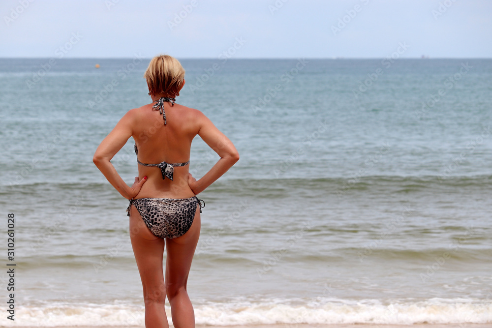 Slim mature woman in leopard swimsuit going to swim in a sea. Concept of  body care, wellness and beach vacation Stock Photo | Adobe Stock