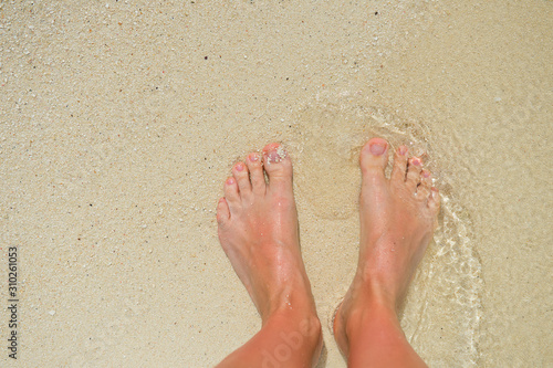 Bare feet on white sand under wave of crystal clear water