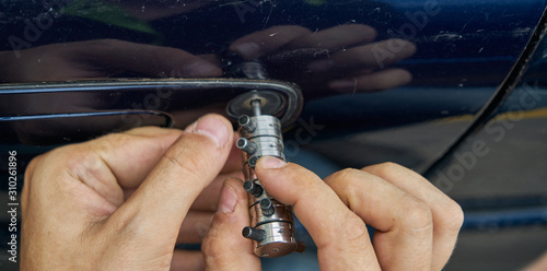 Locksmith opening with the lockpicker a blue car that its owner has lost the keys