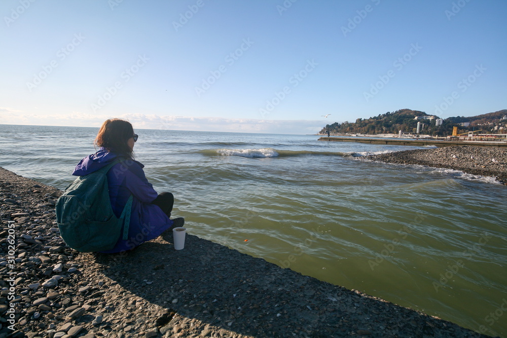 A young woman sits on the shore of the Black sea, Sochi, Russia