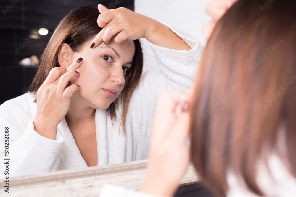portrait of a beautiful girl, in the reflection of the mirror. Fingers remove acne on the face. portrait of a beautiful girl, in the reflection of the mirror. Fingers remove acne on the face.