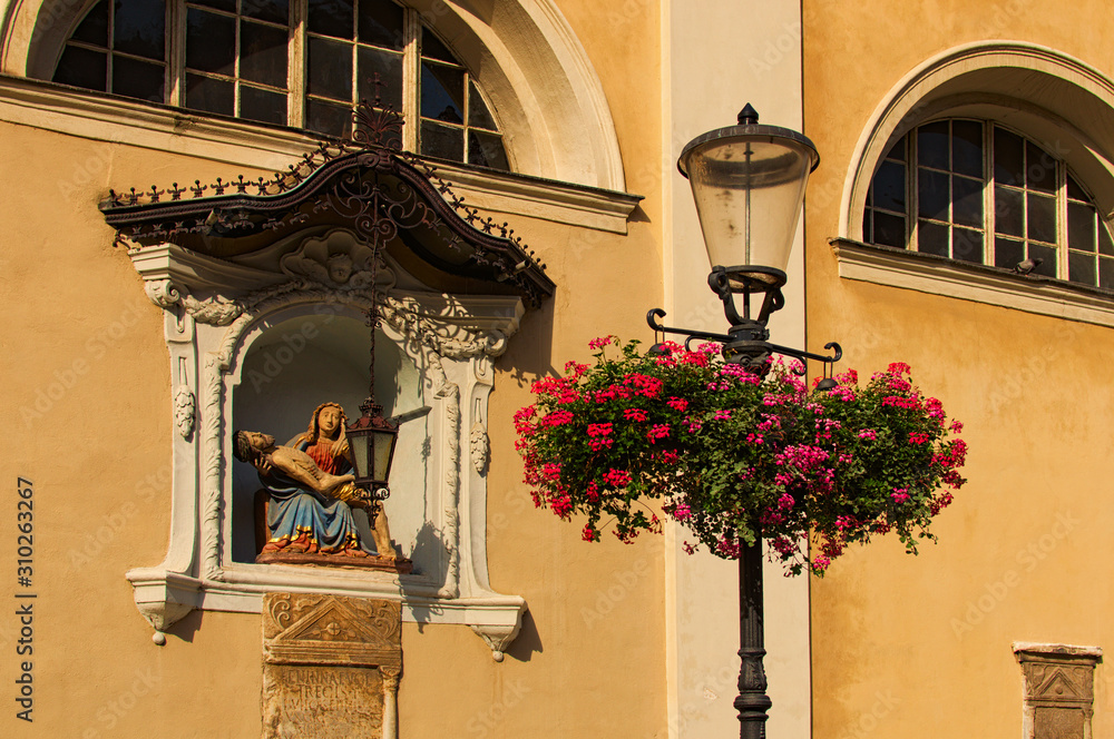 Ljubljana, Slovenia-September 29, 2019: Medieval facade of St. Nicholas's Church at Cyril and Methodius Square. Decorated by Bible?s scene. Ancient lantern with flowers on the pot in the foreground