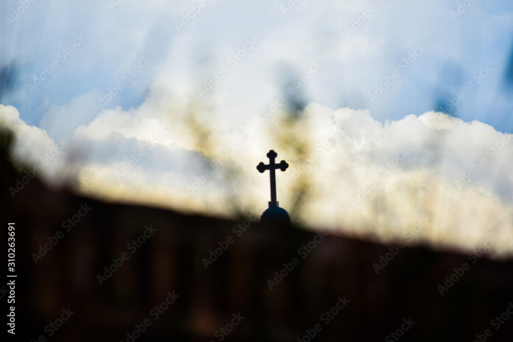 Shadow of a cross seen through grassland with cloudy sky background