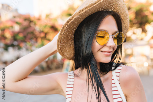 Close-up portrait of dreamy lovely lady with tanned skin posing with eyes closed on nature background. Amazing young woman in yellow glasses thinking about something pleasant on summer resort.