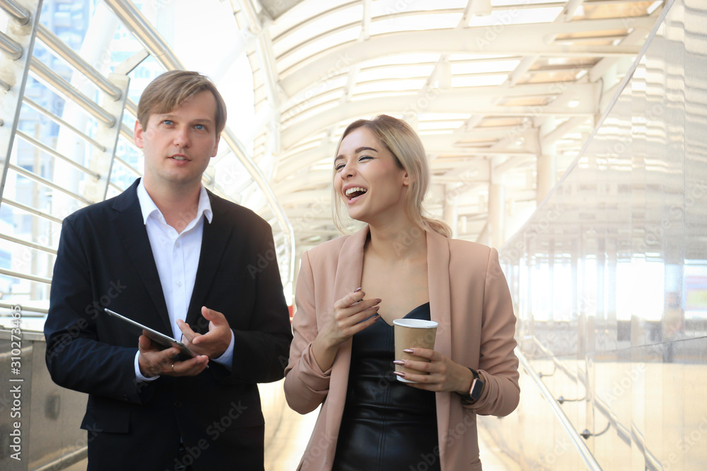 Businessman and businesswoman discussing while walking outside office in modern city. Business colleague discussing about their job on the way, man holding digital tablet and woman drinking morning co
