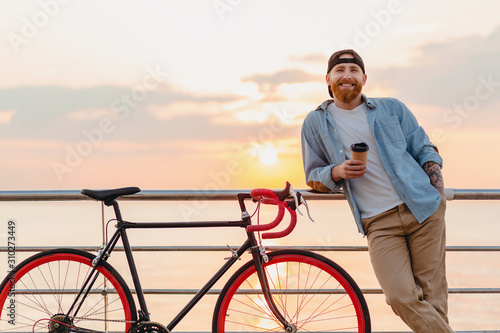 young bearded man traveling on bicycle at sunset sea