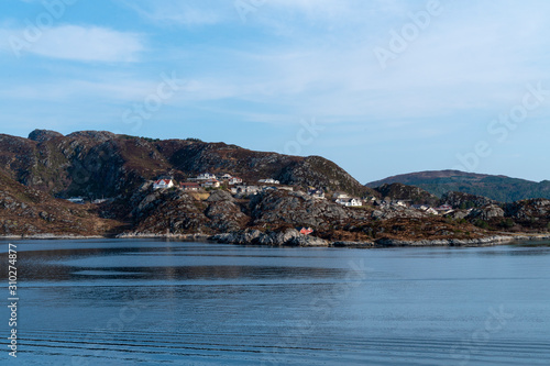 fishing village with colorful wooden fishing huts in the fjords of Norway on a sunny day in spring within a beautiful landscape shot from a boat 