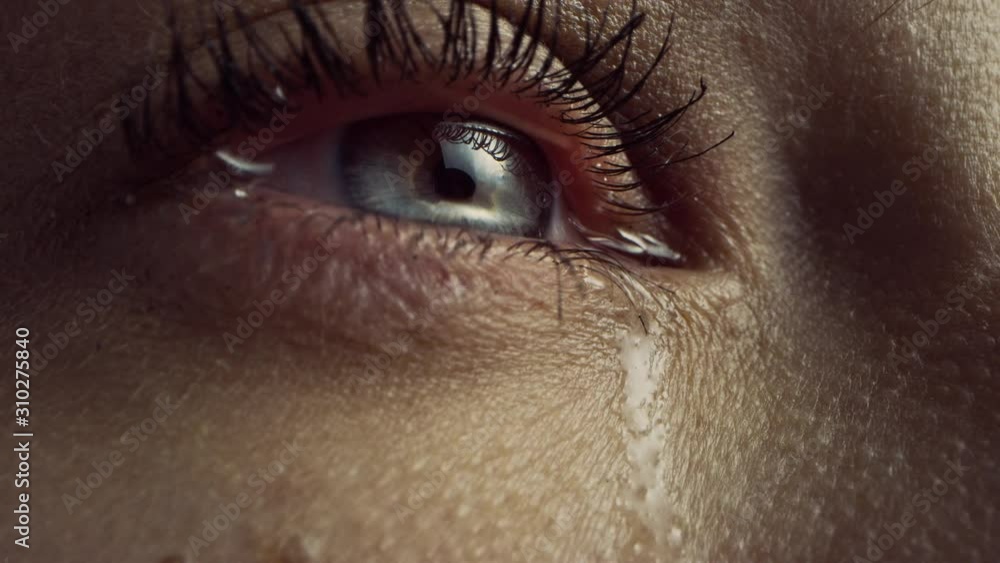 Close Up Macro Zoom Shot of a Crying Eye. Young Beatiful Female with Natural Light Blue, Yellow and Brown Color Pigmentation on the Iris. Mascara is Applied to Eyelashes. Tears are Flowing Down.
