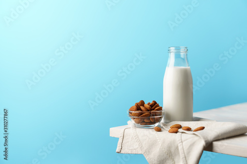 Glass reusable bottle with almond milk, almond nuts lie nearby, textile napkin on a white wooden table and a blue background. photo