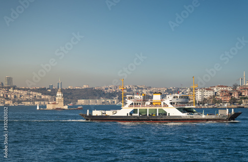 A car ferry full of vehicles, floats through the waters of the Bosphorus on background of Maiden Tower and Istanbul-city.