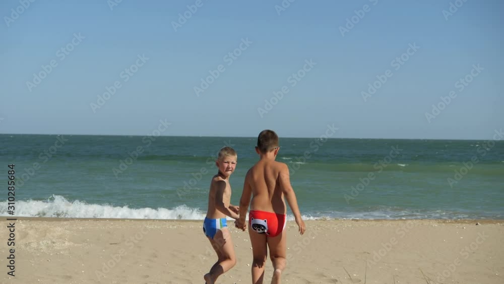 Children run along the coastline. Waves wash over the beach. Boys holding hands running along the beach. The kid in the glasses on the rest of the sea. The boy runs and turns back. Children run along the coastline. Waves wash over the beach. Boys holding hands running along the beach. The kid in the glasses on the rest of the sea. The boy runs and turns back.