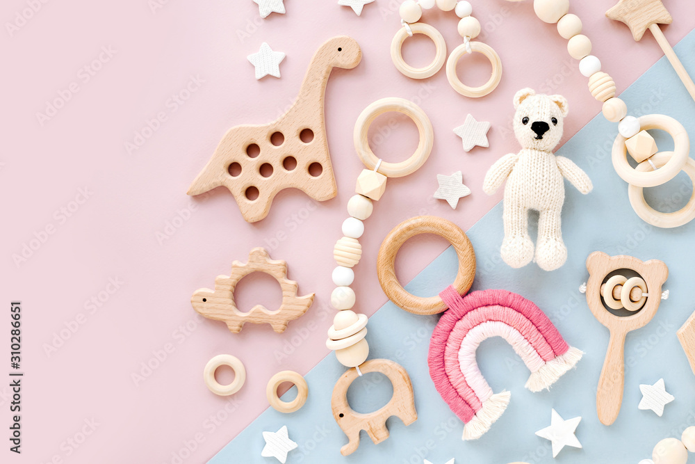 Naklejka premium Cute wooden baby toys on pink and light-blue background. Knitted bear, rainbow, dinosaur toy, beads and stars. Eco accessories, beanbag and teethers for newborn. Flat lay, top view
