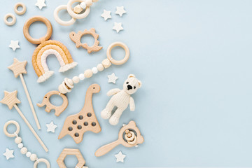 Cute wooden baby toys on light-blue background. Knitted bear, rainbow, dinosaur toy, beads and stars. Eco accessories,  beanbag and teethers for newborn. Blank space for text. Flat lay, top view