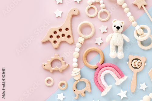Cute wooden baby toys on pink and light-blue background. Knitted bear, rainbow, dinosaur toy, beads and stars. Eco accessories,  beanbag and teethers for newborn. Flat lay, top view