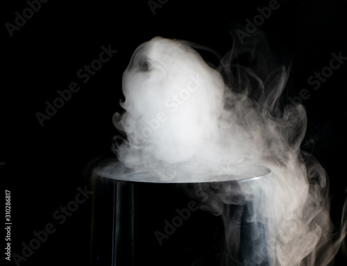 Puffs of white smoke randomly rising rise from the chimney partially flowing down its edges on a black background